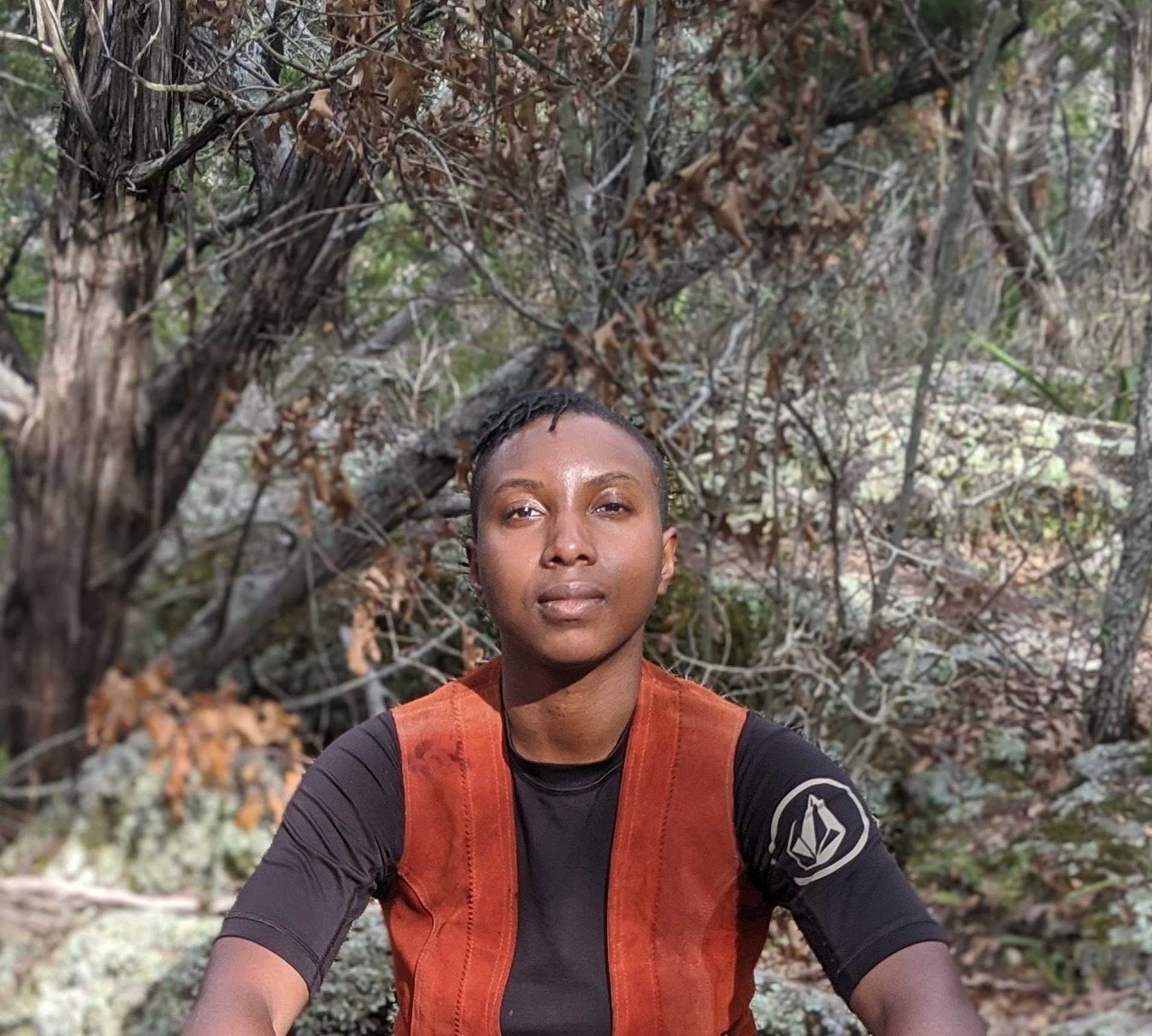 Portrait of Oré Akinsanmi, face shot with hand in prayer position in front of lips. Umber brown skin wit short tightly curled hair. Pensive dark brown eyes looking forward